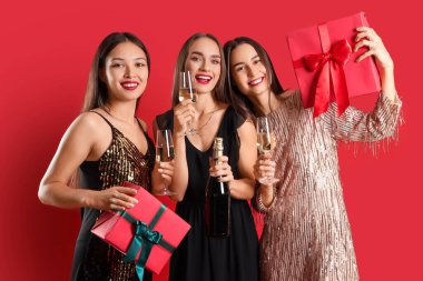 Şampanya ve kırmızı arka planda hediyeleri olan güzel genç kadınlar. Yeni yıl kutlaması