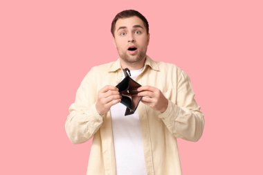 Pembe arka planda boş cüzdanlı, şok olmuş genç bir adam.