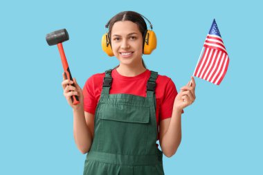 Kulaklık, lastik çekiç ve mavi arka planda Amerikan bayrağı olan kadın inşaat işçisi.