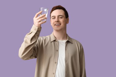 Handsome young man with glass of clean water on lilac background