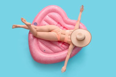 Mayo giymiş güzel bir kadın mavi arka planda şişme yatakta yatıyor.