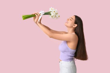 Pembe arka planda bir buket beyaz nergis çiçeğiyle güzel bir genç kadın.