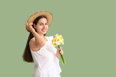 Yeşil arka planda bir buket nergis çiçeğiyle güzel genç bir kadın.