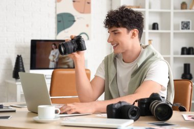 Modern kameraları ve laptopu olan profesyonel mutlu erkek fotoğrafçı stüdyoda çalışıyor.