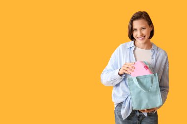 Güzel, genç, mutlu bir kadın. Çantasıyla ve yemek kutusuyla. Sarı arka planda.