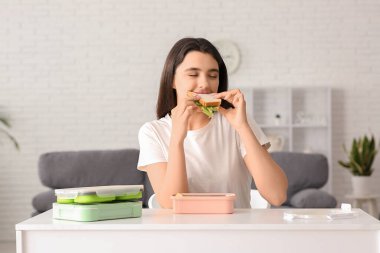 Güzel, genç ve mutlu bir kadın. Beslenme çantaları dolusu lezzetli sandviçleri evde yiyor.