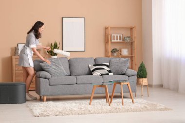 Genç oda hizmetçisi odada toz bezi ile kanepeyi temizliyor.