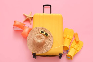 Denizyıldızlı bavul, şişme kol bantları, paletler ve pembe arka planda plaj aksesuarları.