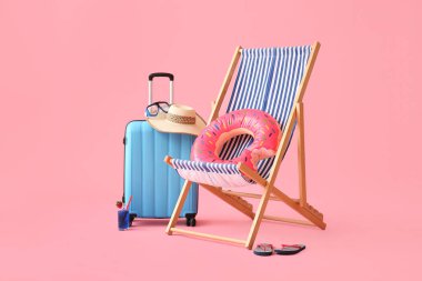 Güverte sandalyesi, bavulu ve pembe arka planda plaj aksesuarları olan şişme bir yüzük.