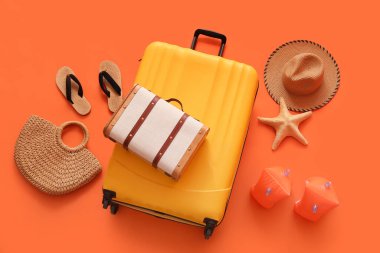 Deniz yıldızlı bavullar, saman torbası ve turuncu arka planda plaj aksesuarları.