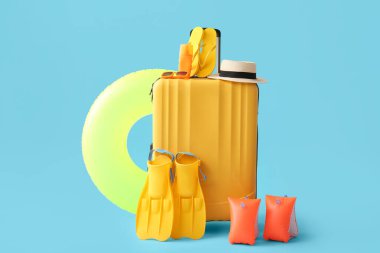 Şişme yüzüklü bavul, kolluk, palet ve mavi arka planda plaj aksesuarları.