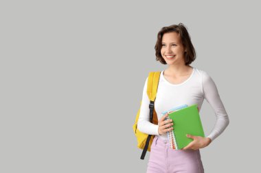 Gri arkaplan üzerine not defterleri ve sırt çantasıyla güzel bir kız öğrenci.