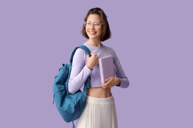 Sırt çantası ve eflatun arkaplan üzerine kitabı olan güzel bir kız öğrenci.