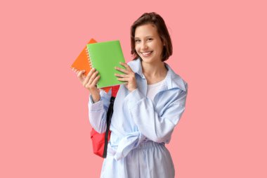 Sırt çantası ve pembe arka planda defterleri olan güzel bir kız öğrenci.