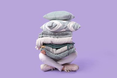 Mor arka planda oturan bir yığın farklı battaniye ve yastıkla güzel bir genç kadın.