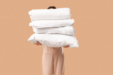 Bej arka planda bir yığın farklı battaniyesi olan güzel genç bir kadın.