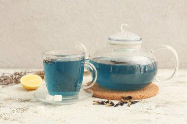 Bir fincan kelebek çiçeği çayı ve arkaplanda çaydanlık.