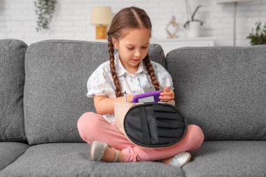 Evdeki kanepede oturan kozmetik çantalı tatlı küçük kız.