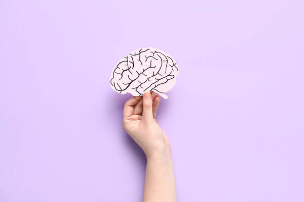Female hand with paper human brain on lilac background