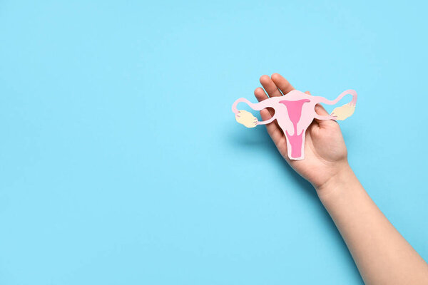 Female hand with paper uterus on color background, closeup