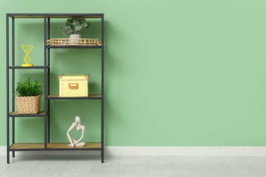 Salonda yeşil duvarın yanında saksı, kutu ve heykelcik olan raf ünitesi.