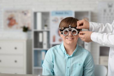 Kadın göz doktoru klinikte göz testi yaptıran küçük çocuğa yardım ediyor.