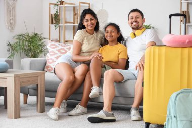 Happy family with packed suitcase for travel sitting on sofa at home clipart