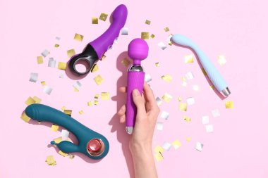 Pembe arka planda farklı seks oyuncakları olan bir kadın eli.