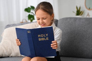Evdeki kanepede İncil okuyan tatlı küçük kız.