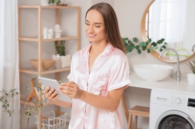 Banyoda tablet bilgisayar kullanan genç bir kadın.