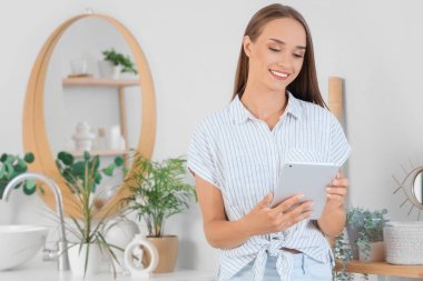 Çamaşır odasında tablet bilgisayarı olan genç bir kadın.