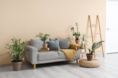 Oturma odasının iç tarafındaki bej duvarın yanında rahat bir kanepe, merdiven ve bitkiler.