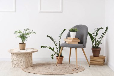 Masa, sandalye, kitaplar ve oturma odasındaki beyaz duvarın yanındaki farklı bitkiler.