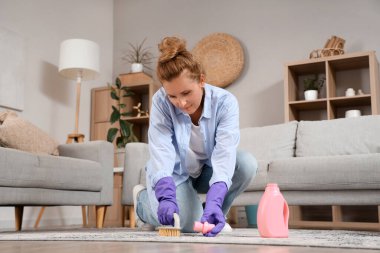 Evde fırçası ve deterjanı olan olgun bir kadın var.