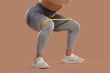 Kahverengi arka planda esnek bant olan kadın vücut geliştirici eğitimi