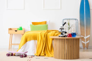 Genç kızın yatak odasındaki masada kimyasal şişelerle modern mikroskop.