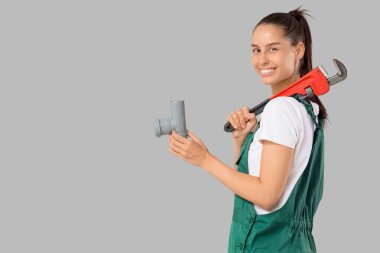 Hafif arka planda İngiliz anahtarı ve borusu olan kadın tesisatçı.