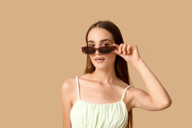 Kahverengi arka planda şık güneş gözlüklü güzel bir kadın.