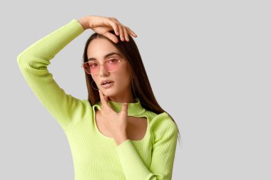 Gri arka planda pembe güneş gözlüklü güzel bir kadın.