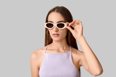 Gri arka planda şık güneş gözlüklü güzel bir kadın.