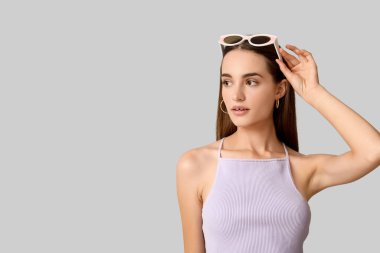 Gri arka planda şık güneş gözlüklü güzel bir genç kadın.