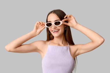 Gri arka planda şık güneş gözlüklü mutlu genç kadın.