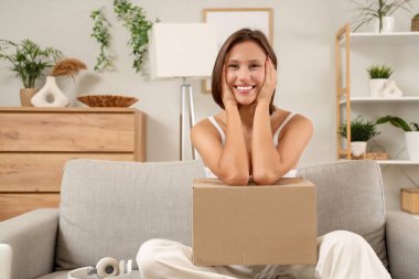 Güzel, genç, mutlu bir kadın. Paketi evde, koltukta oturuyor.