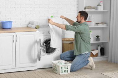 Genç adam çamaşır makinesinden temiz çamaşır alıyor.