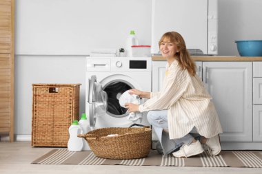 Evde çamaşır makinesinden temiz çamaşır alan genç bir kadın.