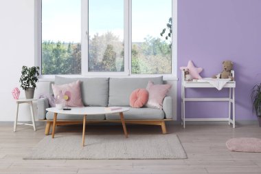 Kanepe, kahve masası ve şık çocuk odasında menekşe duvarının yanındaki masaları değiştirmek.