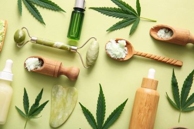 Deniz tuzu, yüz masajı aletleri ve yeşil arka planda yapraklarla kenevir kozmetik yağı şişeleri.