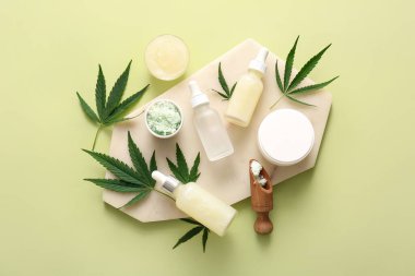 Yeşil zemin üzerinde deniz tuzu, yaprak ve krema bulunan kenevir kozmetik yağı şişeleri