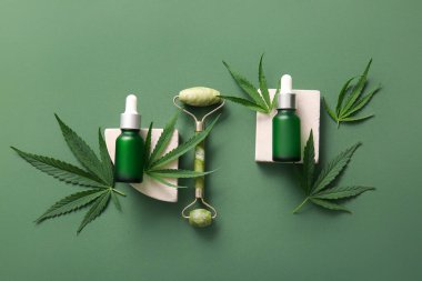 Bir şişe kenevir kozmetik yağı, masaj rulosu ve yeşil arka planda yapraklar.
