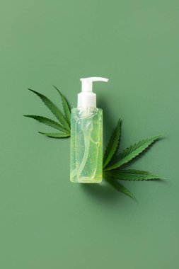 Bir şişe kenevir kozmetik ürünü ve yeşil arka planda yapraklar